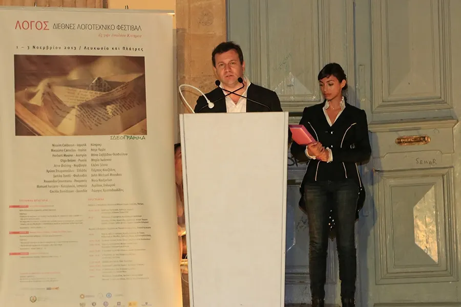 John Michael Mouskos and Kristie Papadopoulou at a lectern at ΛΟΓΟΣ 2013